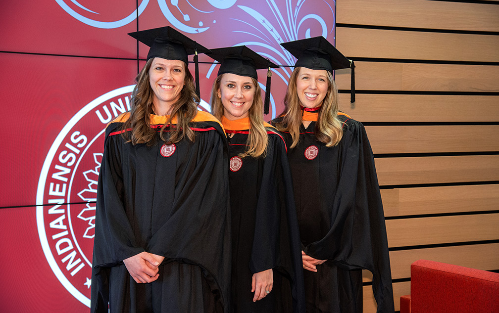 Three smiling graduates in caps and gowns.