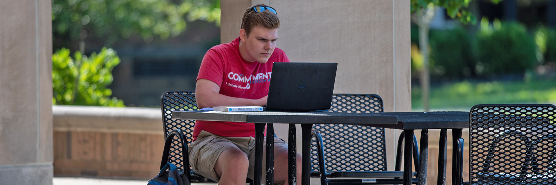 Student completing coursework online, seated outdoors and alone while practicing social distancing.