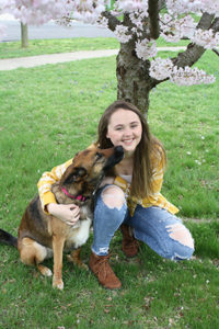 Jillian Splawn sits in front of a flowering tree with a dog