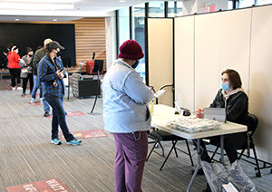 IU East student Nolan Blair welcomes faculty, staff and students to the campus' COVID-19 Mitigation Testing each week in the Whitewater Hall lobby. Blair assists each person as they sign in for testing. Photo is in lobby of Whitewater Hall mitigation testing area including table to sign in, and participants in line.