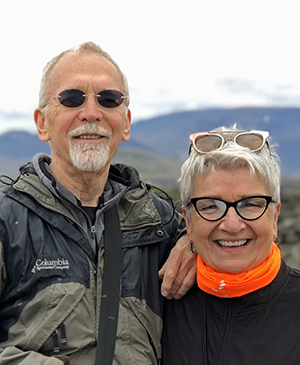 Jerry Logan stands next to his wife Terri Logan in front of a mountain landscape